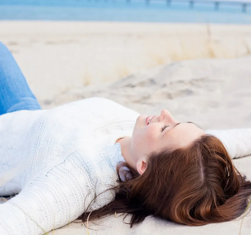 Eine Frau liegt mit ausgestreckten Armen am Strand in Binz und genießt die Meeresbrise der Ostsee.