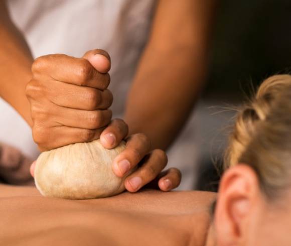 Close-up of a woman receiving a soothing Ayurvedic herbal stamp massage on her back.