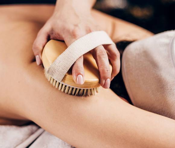 Dry brushing full body massage with copper bristles on a customer's arm to stimulate blood circulation.
