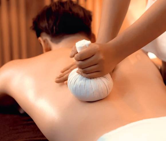 Application of a relaxing herbal stamp massage on the back of a man.