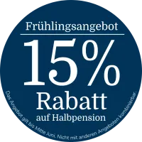 Rundes dunkelblaues Werbebadge mit der Aufschrift „Frühlingsangebot“ auf Deutsch, „15 % Rabatt auf Halbpension“ sowie dem Hinweis, dass das Angebot bis Mitte Juni gültig und nicht mit anderen Angeboten kombinierbar ist.