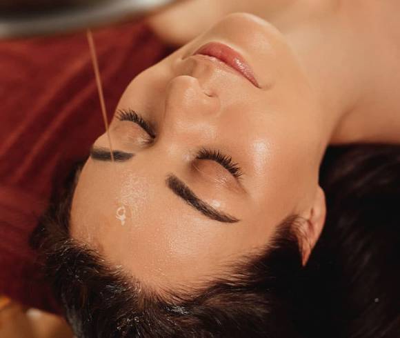 Relaxed woman enjoys Shirodhara treatment with warm herbal oil.
