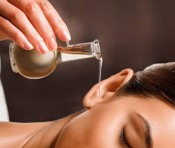 Herbal oil flows into the ear of a contentedly smiling spa guest.