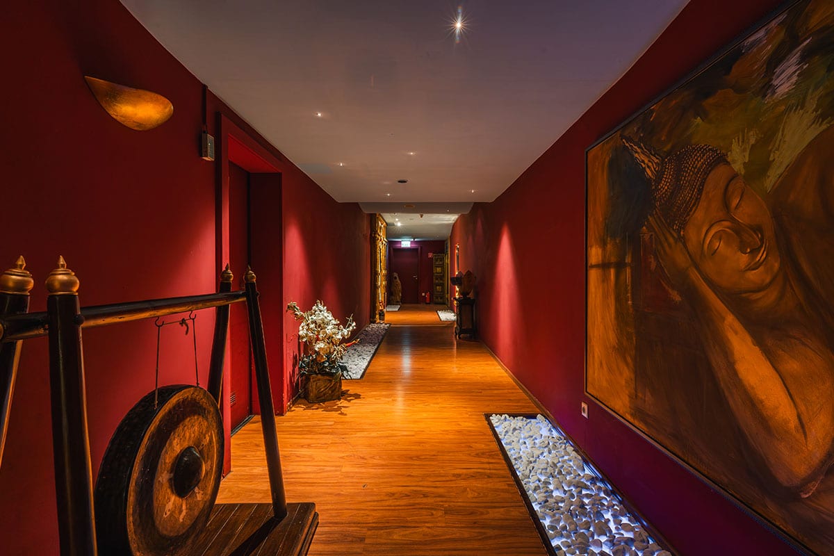 Spa-Flur mit roter Wand, Buddha-Bild, dekorativem Gong und stimmungsvoller Beleuchtung