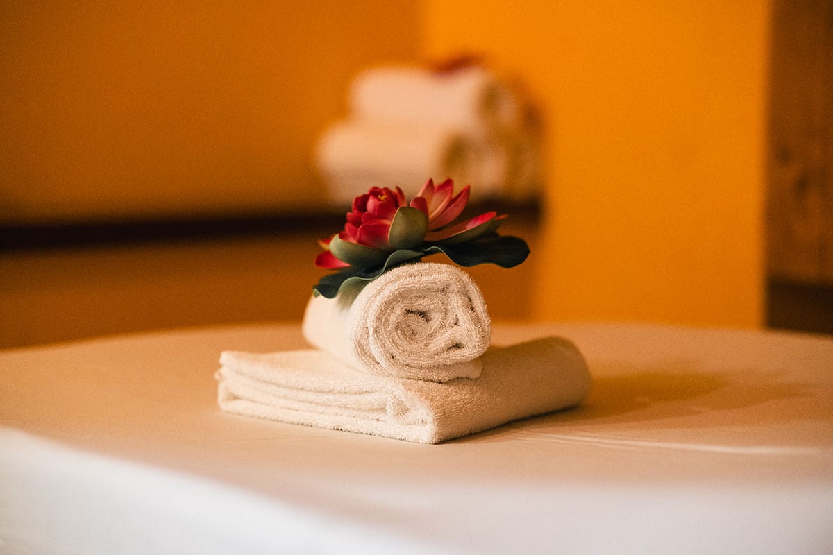 Gefaltetes weißes Handtuch mit roter Lotusblüte auf Massageliege im Spa